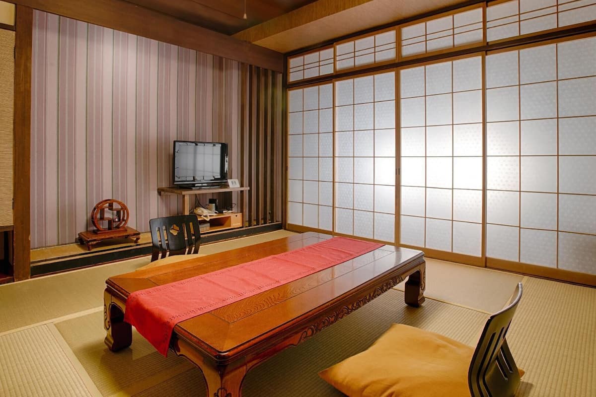 A traditional Japanese room with tatami flooring, a low wooden table, a television, and sliding shoji doors.