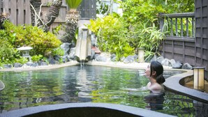 A person in a hot spring surrounded by greenery and a wooden fence. - YUBANA MANKAI (Higashiizu)