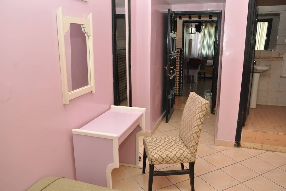 A pink-walled room with a white desk and a patterned chair.