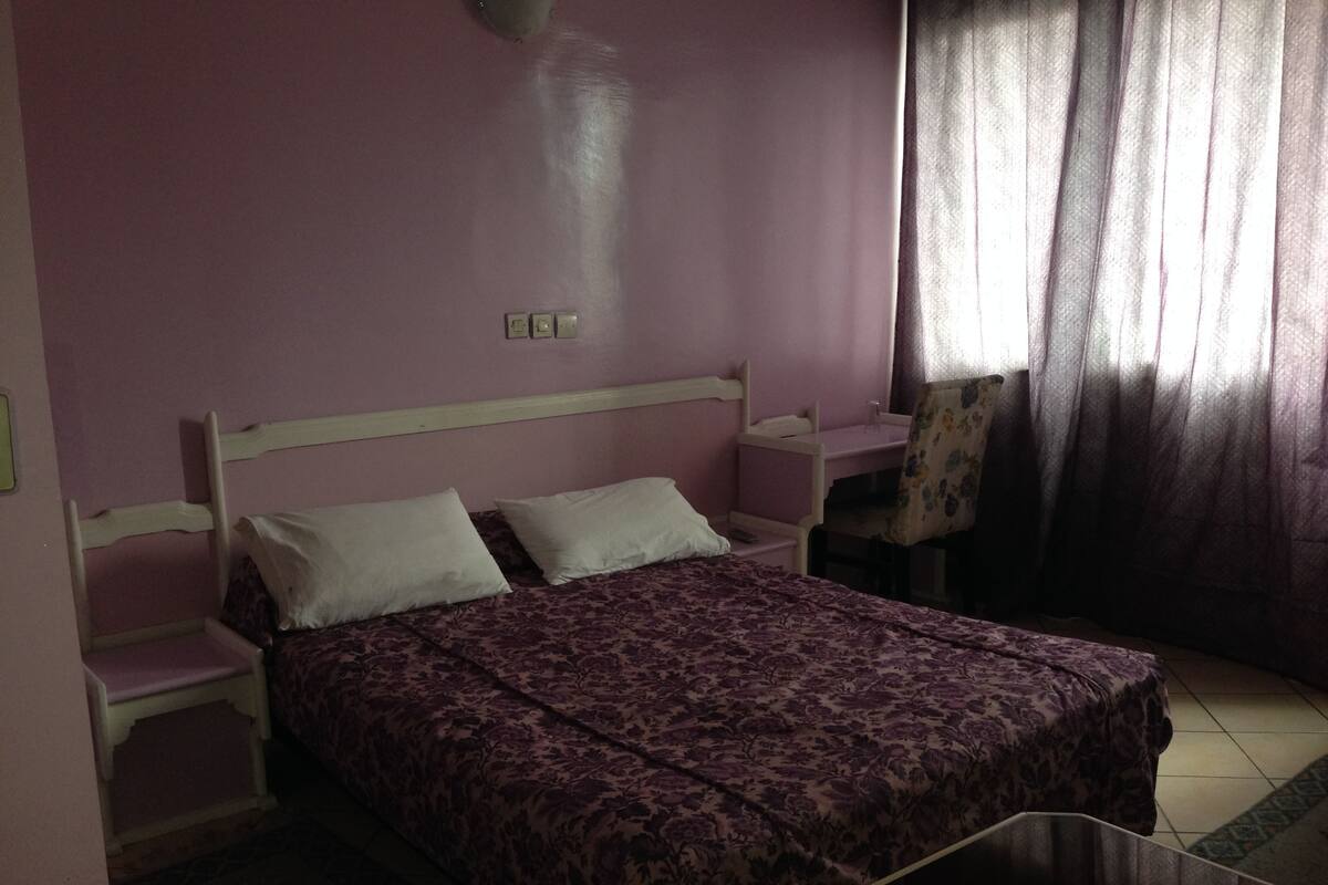 A bedroom with a bed, two nightstands, a chair, and a window with curtains.