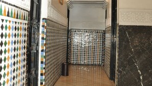 A hallway with patterned tiles, a black door, and a trash can. - Hôtel Boustane (Casablanca)