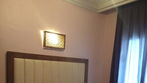 A bedroom with a bed, a nightstand, a wall-mounted light, and a window with curtains. - Hôtel Boustane (Casablanca)