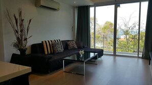 A modern living room with a dark sofa, a glass coffee table, and a view through large windows. - Chan Residence Hua Hin (Hua Hin)