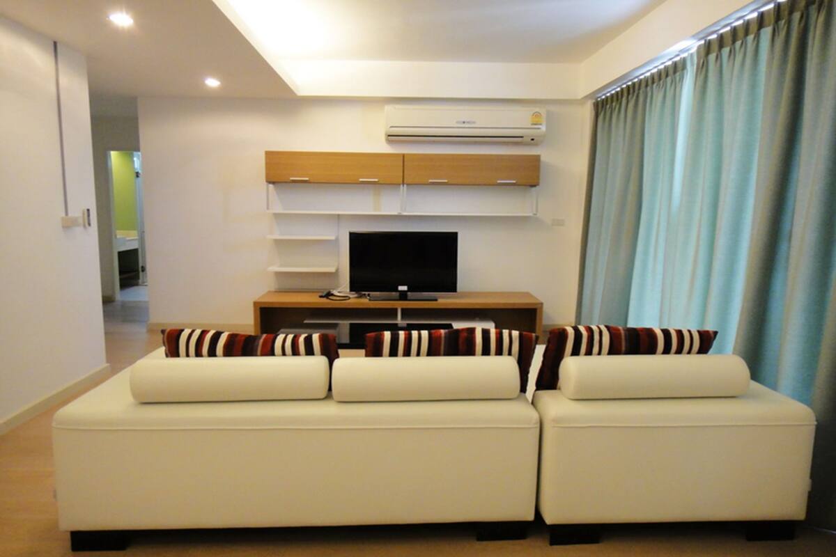 A modern living room with a white sofa set, a flat-screen TV, and a wooden entertainment unit.