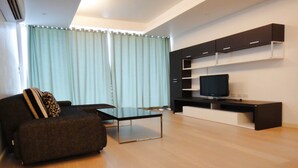 A modern living room with a sofa, a coffee table, a TV on a black stand, and built-in shelving. - Chan Residence Hua Hin (Hua Hin)