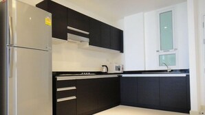 A modern kitchen with dark cabinets, a stainless steel refrigerator, and a microwave on the countertop. - Chan Residence Hua Hin (Hua Hin)