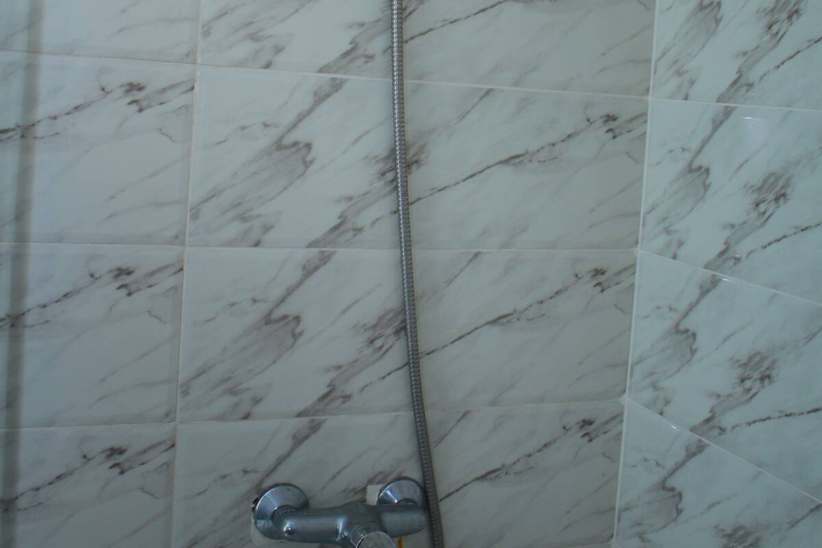 Chuveiro com chuveiro manual e torneira fixada na parede, sobre piso cerâmico.