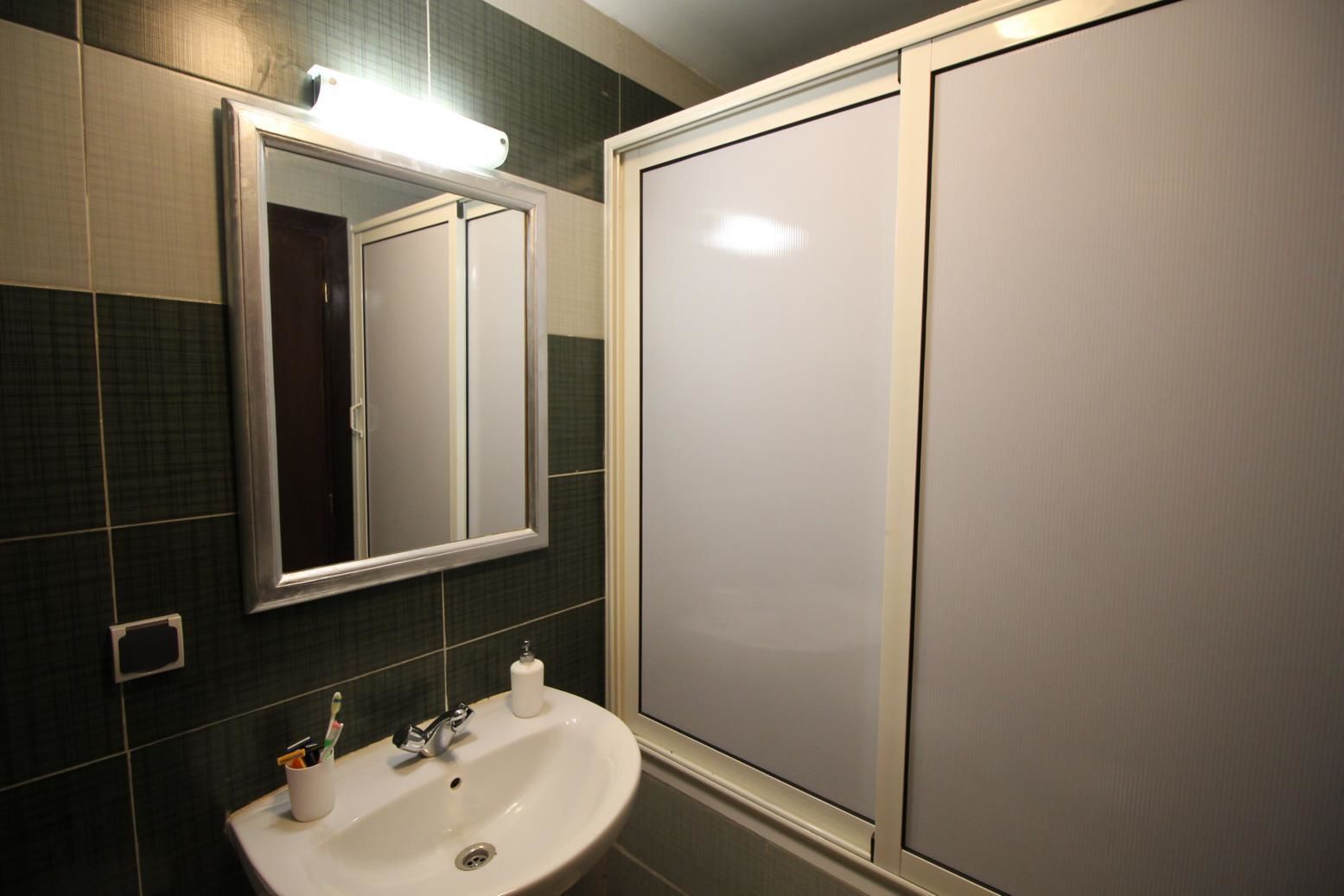Un bany amb un lavabo blanc, un mirall i una cabina de dutxa.