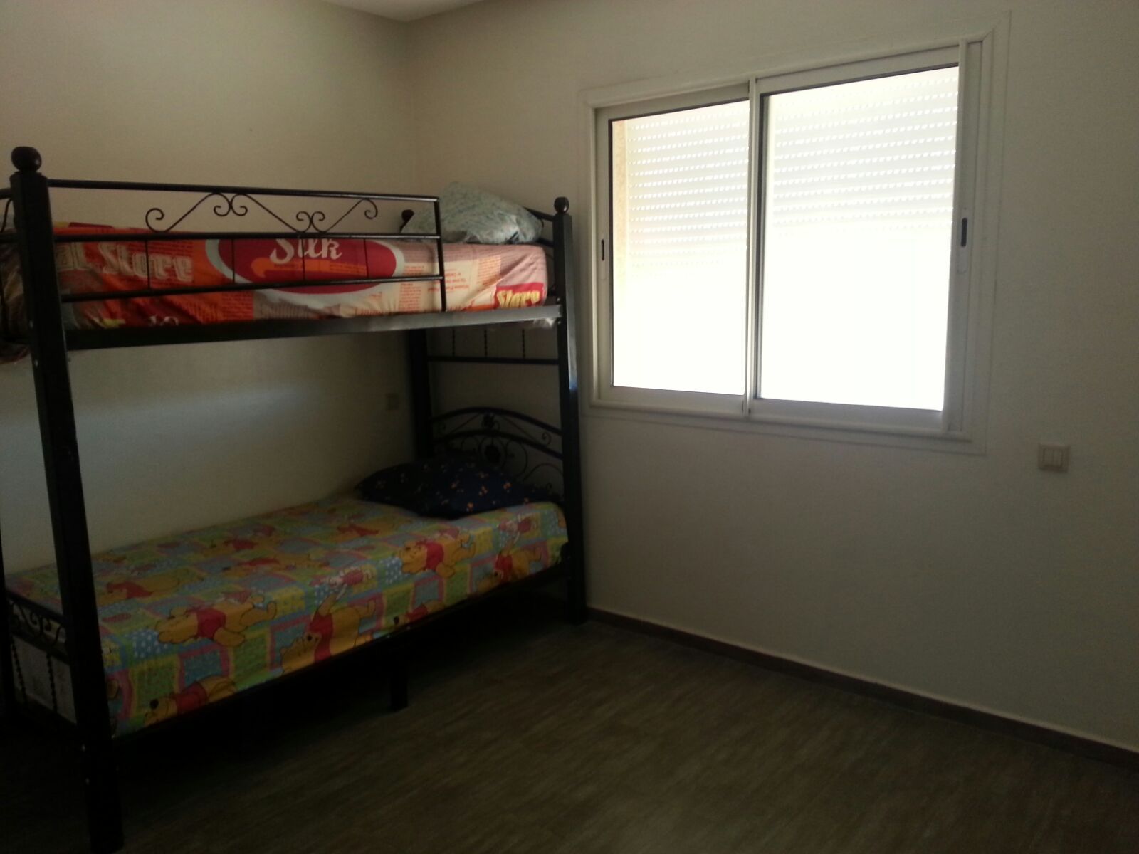 A room with a bunk bed, a window with blinds, and a wooden floor.