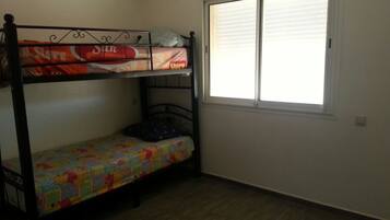A room with a bunk bed, a window with blinds, and a wooden floor.