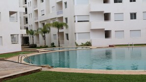 Una piscina rodeada por un edificio blanco con balcones y un área verde.