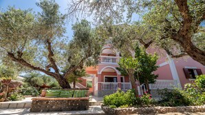 A building with a pink facade, a white balcony, and a stone bench in the foreground. - Arazzo Apartments (Zakynthos)