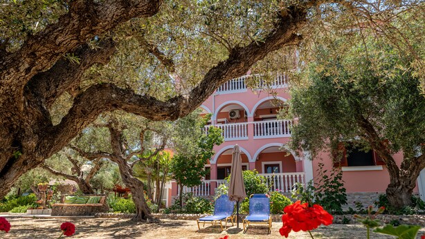 A building with a pink facade, a balcony, and a garden with trees and flowers. - Arazzo Apartments (Zakynthos)