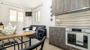 A modern kitchen with a built-in oven, a dining table with chairs, and a sofa. - Arazzo Apartments (Zakynthos)