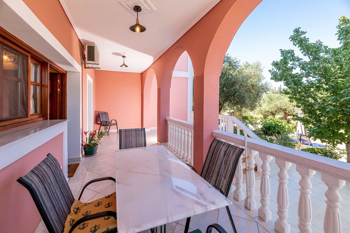 A balcony with a white railing, a table with chairs, and a potted plant.