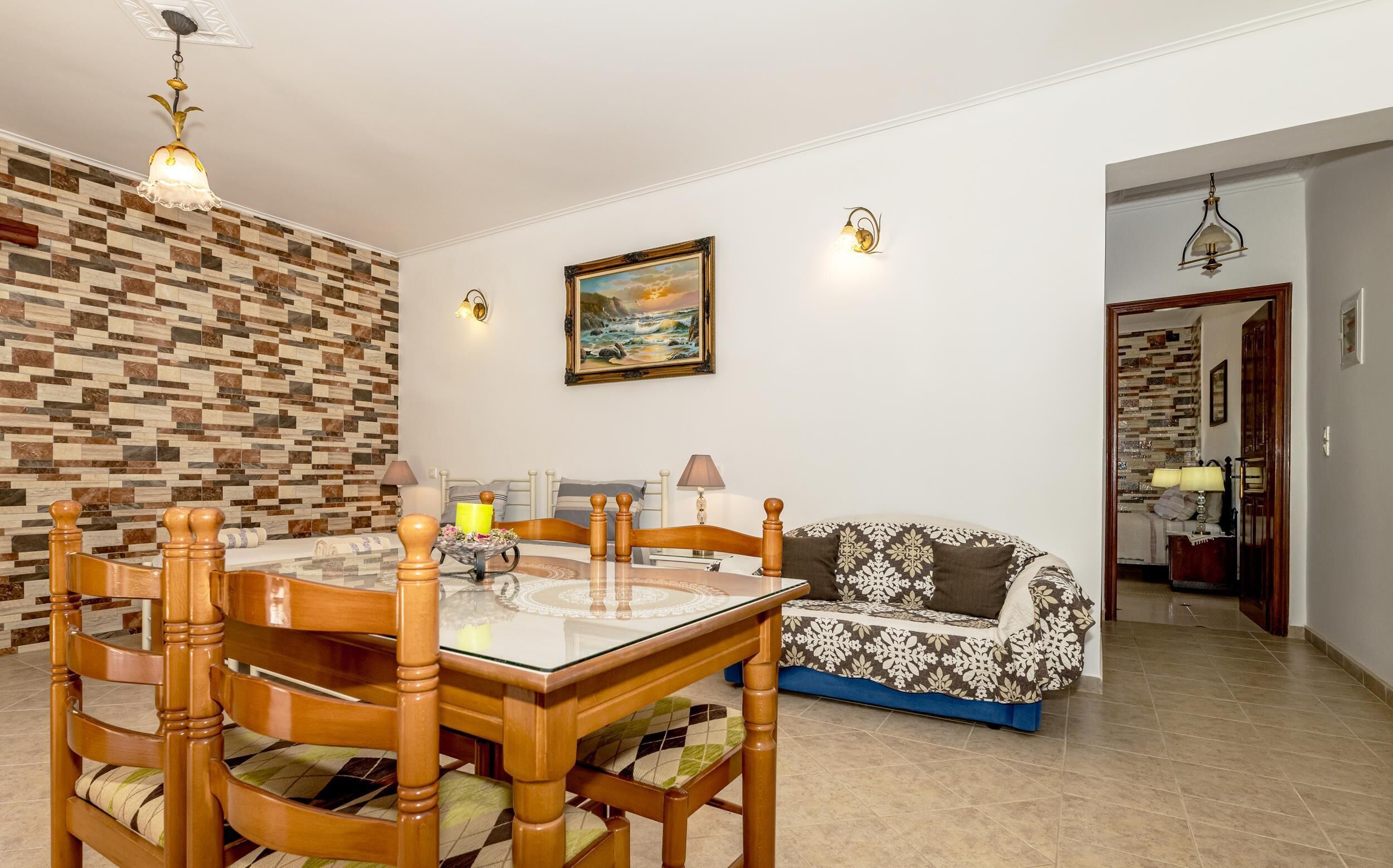 A dining area with a wooden table and chairs, a patterned wall, a sofa, and a painting on the wall.