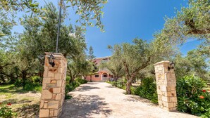 A stone pathway leading to a building with a red roof, surrounded by olive trees and greenery. - Arazzo Apartments (Zakynthos)