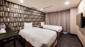 Habitación de hotel con dos camas, una estantería, un escritorio, un televisor y una ventana con cortinas.