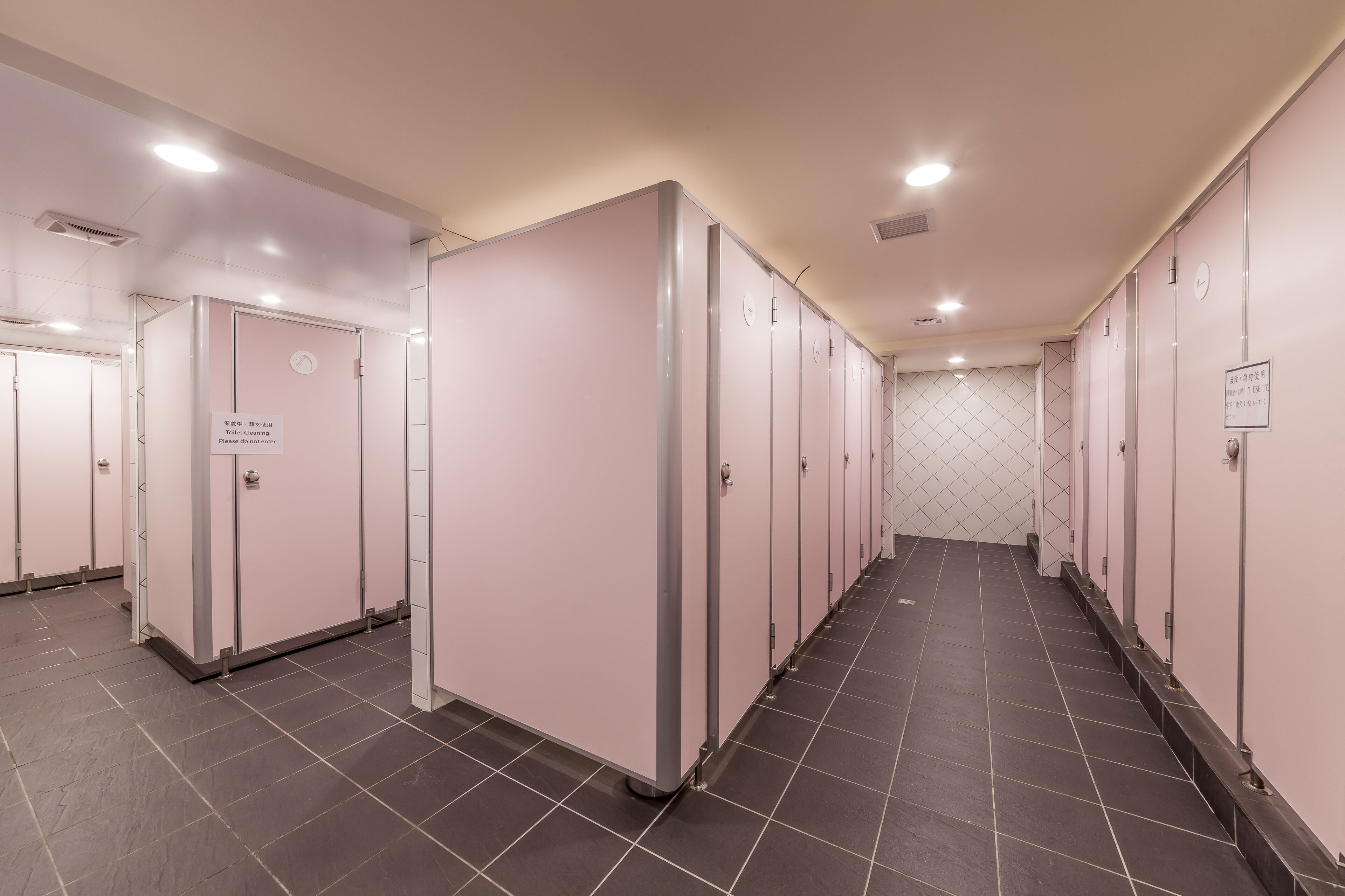 A clean, modern restroom with multiple stalls, each with a privacy partition and a sign indicating usage instructions.