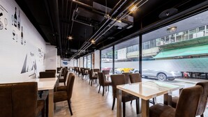 Un restaurante con una barra larga, sillas marrones y amplios ventanales con vistas a la calle.