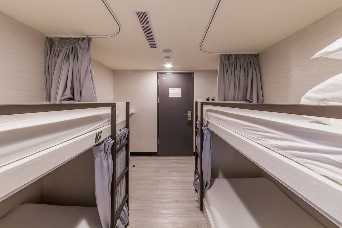 A hotel room with bunk beds, a door with a sign, and a light fixture on the ceiling.