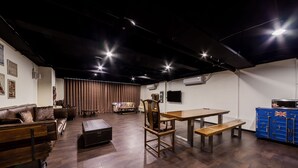 Una habitación amplia con suelo de madera, un sofá de cuero marrón, una mesa de comedor de madera con bancos y un mueble de almacenamiento azul con una bandera Union Jack.