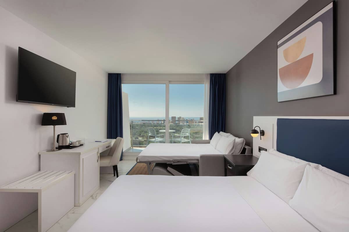 Habitación de hotel moderna con cama, escritorio y un amplio ventanal con vistas a la ciudad.