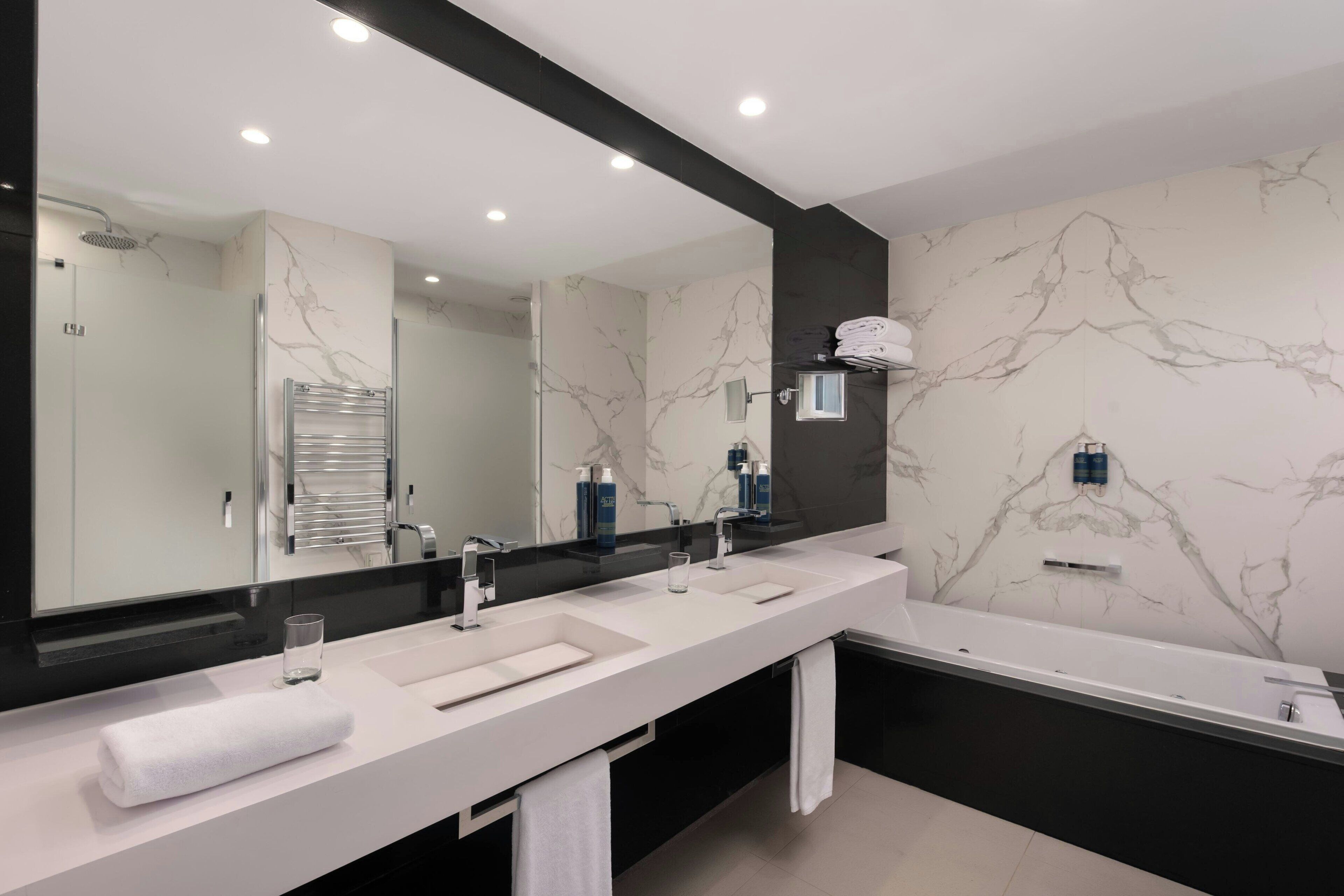 A modern bathroom with a long vanity, two sinks, a large mirror, and a bathtub.