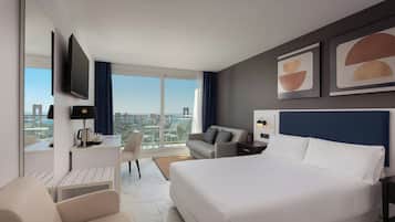 Una habitación de hotel moderna con una cama grande, un escritorio con silla, un sofá y un televisor montado en la pared.