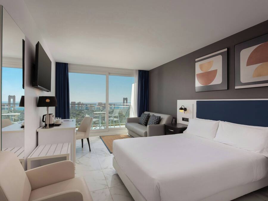 Una habitación de hotel moderna con una cama grande, un escritorio con silla, un sofá y un televisor montado en la pared.