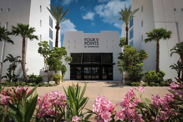 En hotellentrén med en skylt som visar texten ”FOUR POINTS BY SHERATON”, omgiven av palmer och blommor.