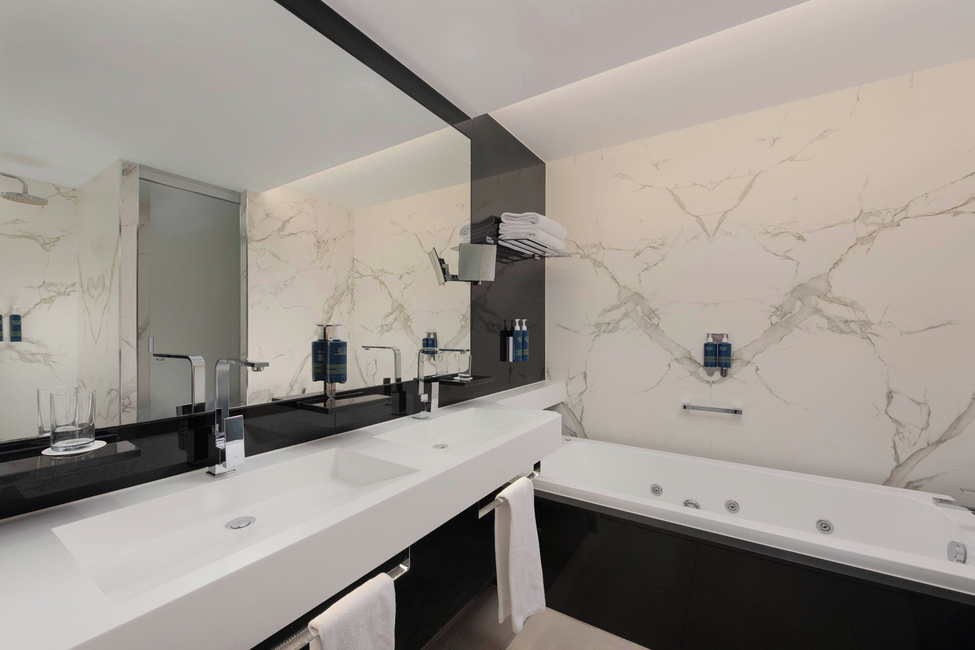 A modern bathroom with two sinks, a large mirror, and a bathtub.