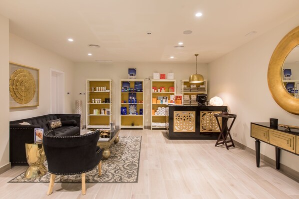 Una sala de estar moderna con un sofá negro, una mesa de centro y un sillón negro. Hay estanterías con varios objetos y un escritorio con una lámpara.