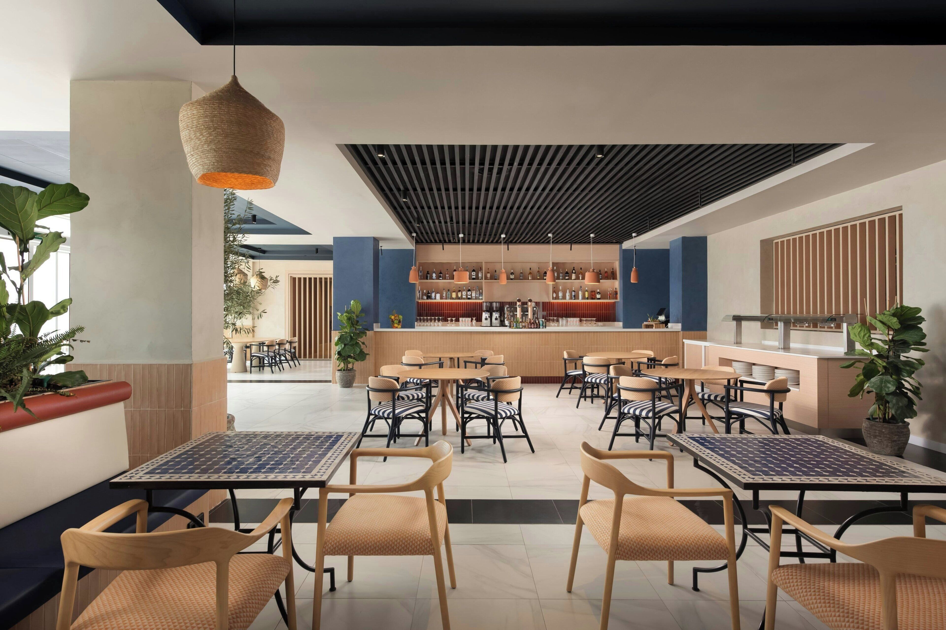 Una cafetería moderna con varias zonas de estar, una barra y una gran variedad de plantas.