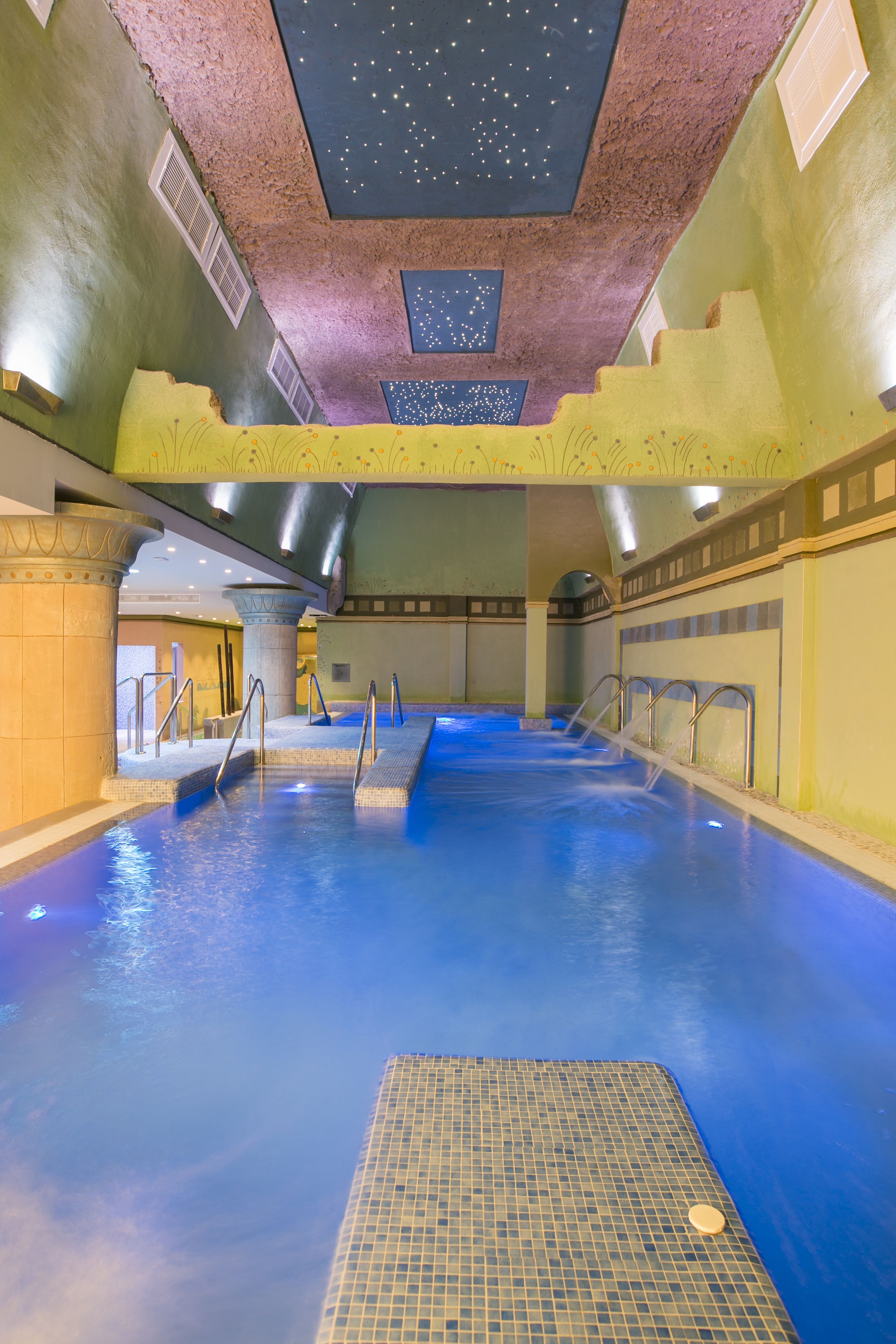 An indoor swimming pool with clear water, multiple entry points, and a ceiling with star projections.