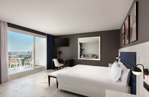 Ett modernt hotellrum med en stor säng, ett skrivbord, en stol och en balkong med utsikt.