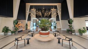 Un lobby espacioso con zona de estar central, plantas en macetas y un mostrador de recepción.