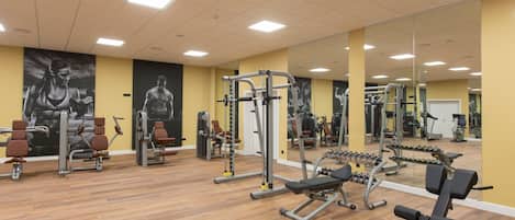 Ett gym med olika typer av träningsutrustning, trägolv och speglade väggar.