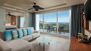 Una habitación de hotel moderna con sofá, una mesa redonda de vidrio, televisor y balcón con vistas.