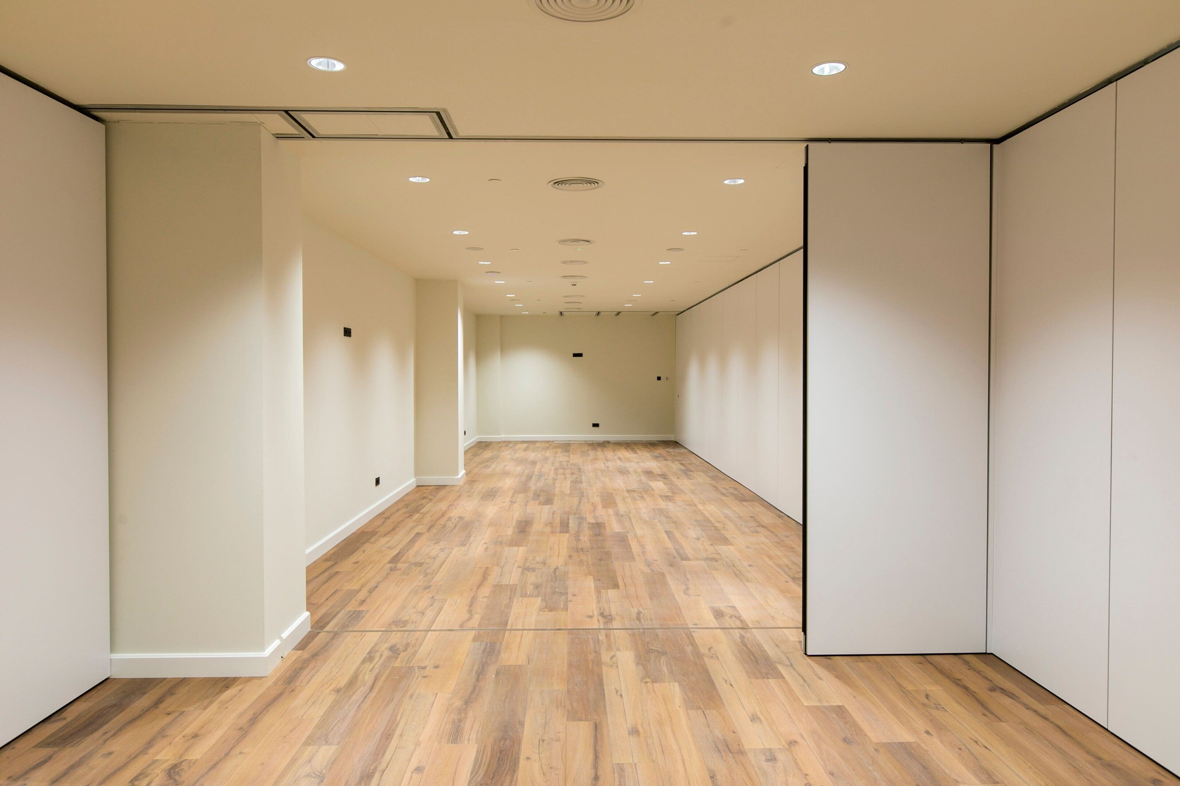 Un estrecho pasillo con suelo de madera y paredes blancas, que conduce a una puerta al final.