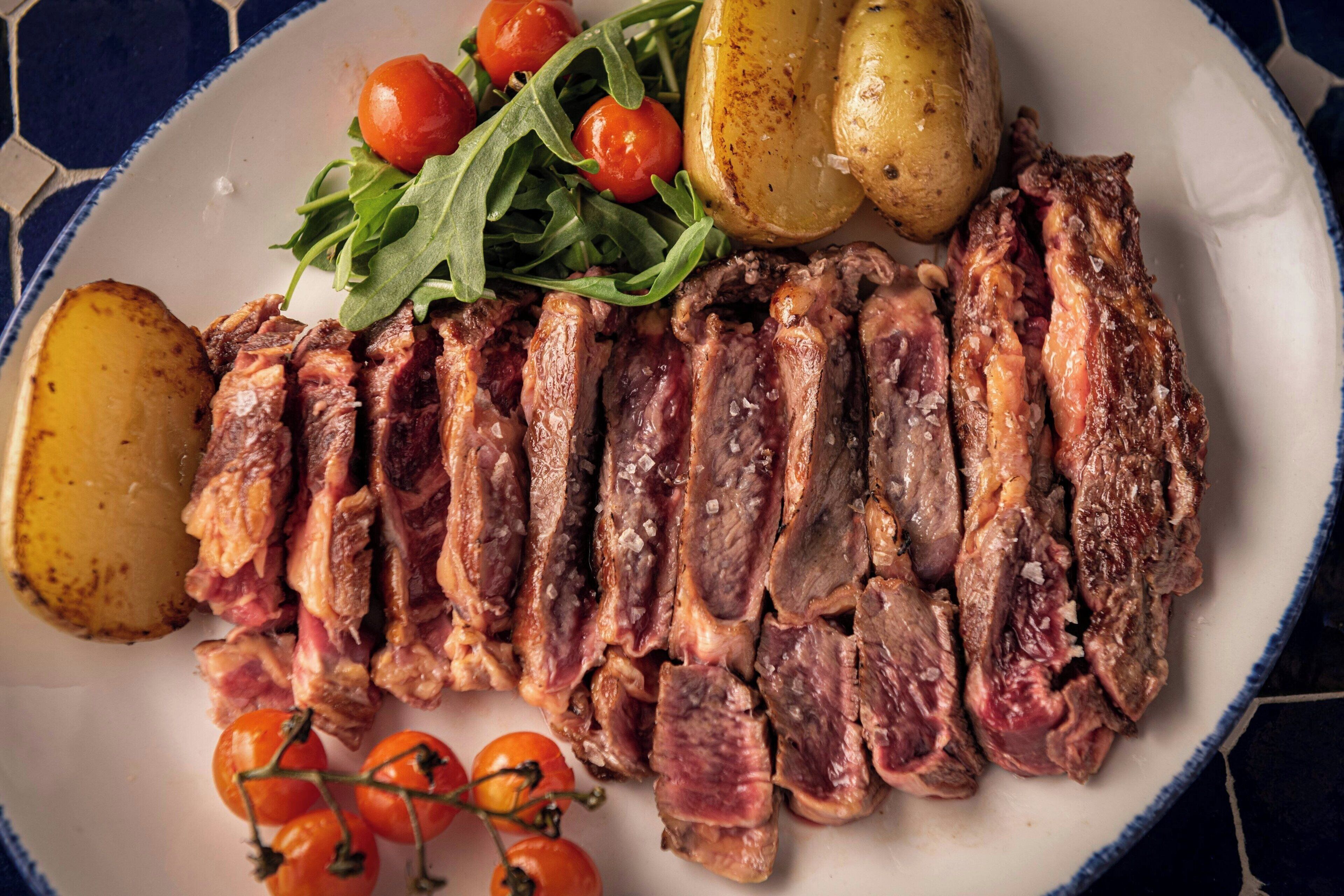A plate of sliced meat, potatoes, and cherry tomatoes.