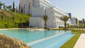 Un hotel moderno con una piscina grande, palmeras y un cielo azul despejado.
