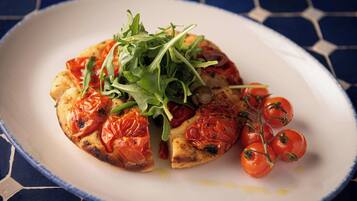 A plate of pizza with tomato slices and greens on a blue and white patterned tablecloth.