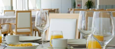 Un comedor con mesas dispuestas para el desayuno, incluyendo platos, vasos y una jarra de jugo.