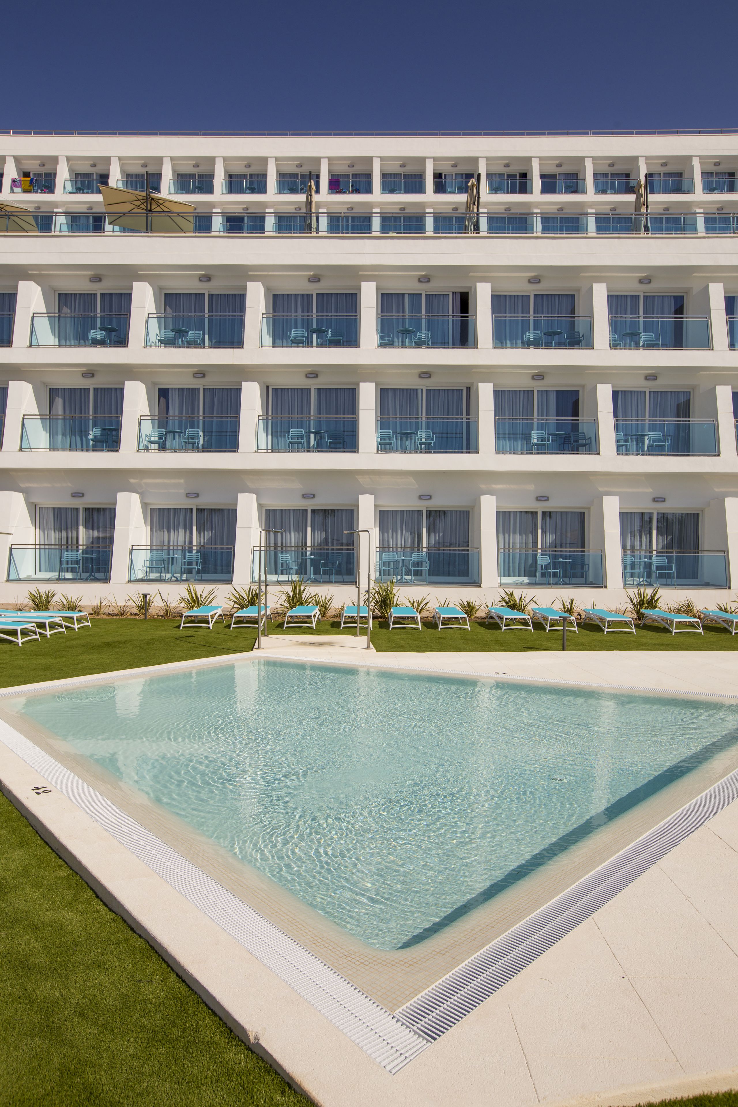 Un hotel con piscina, varios balcones y tumbonas.