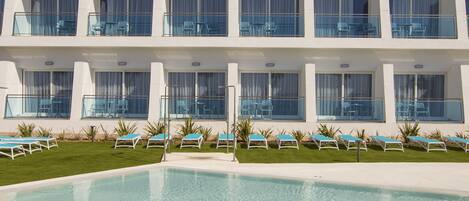 Un hotel con piscina, varios balcones y tumbonas.