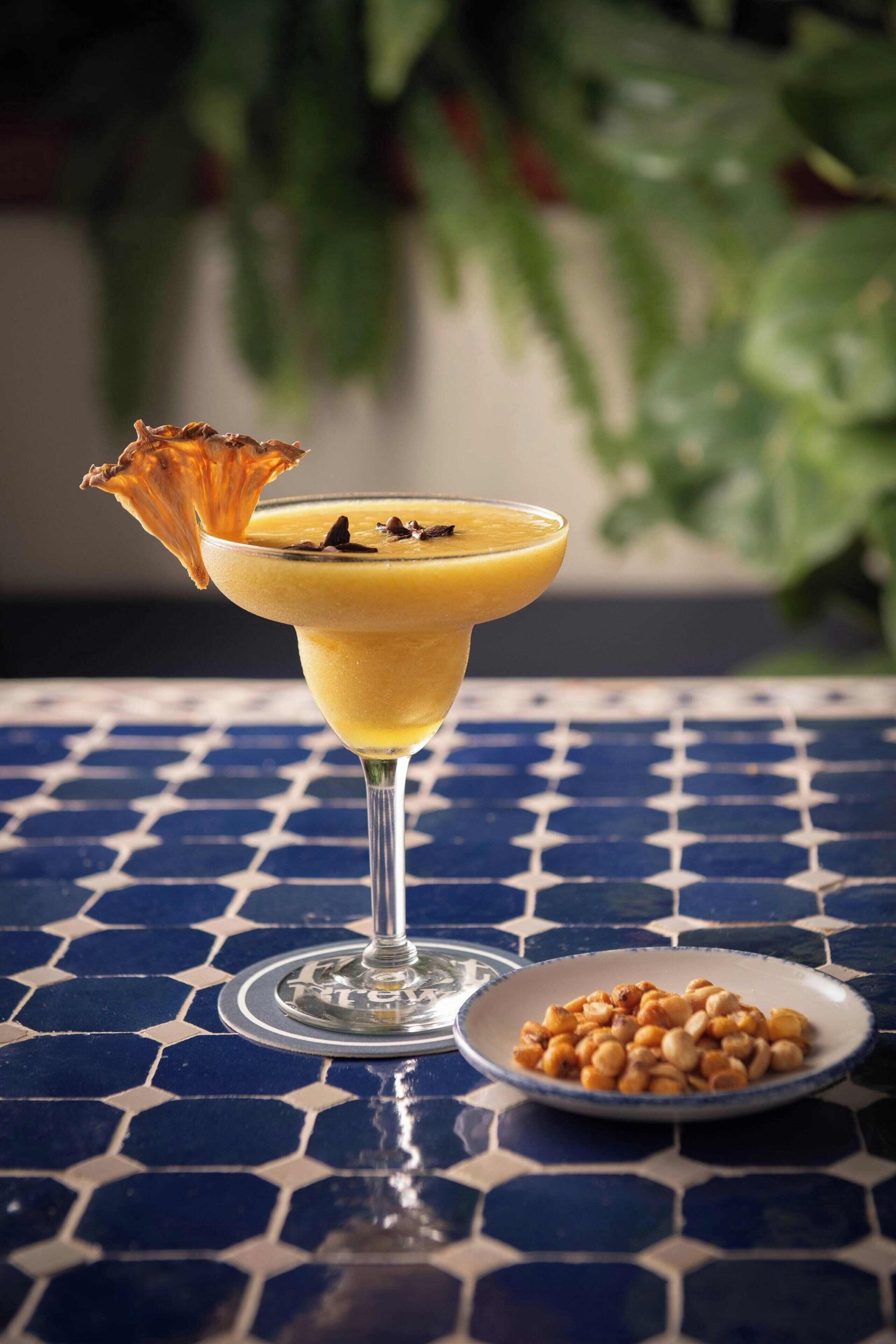 A cocktail in a martini glass with a decorative garnish on a tiled table.