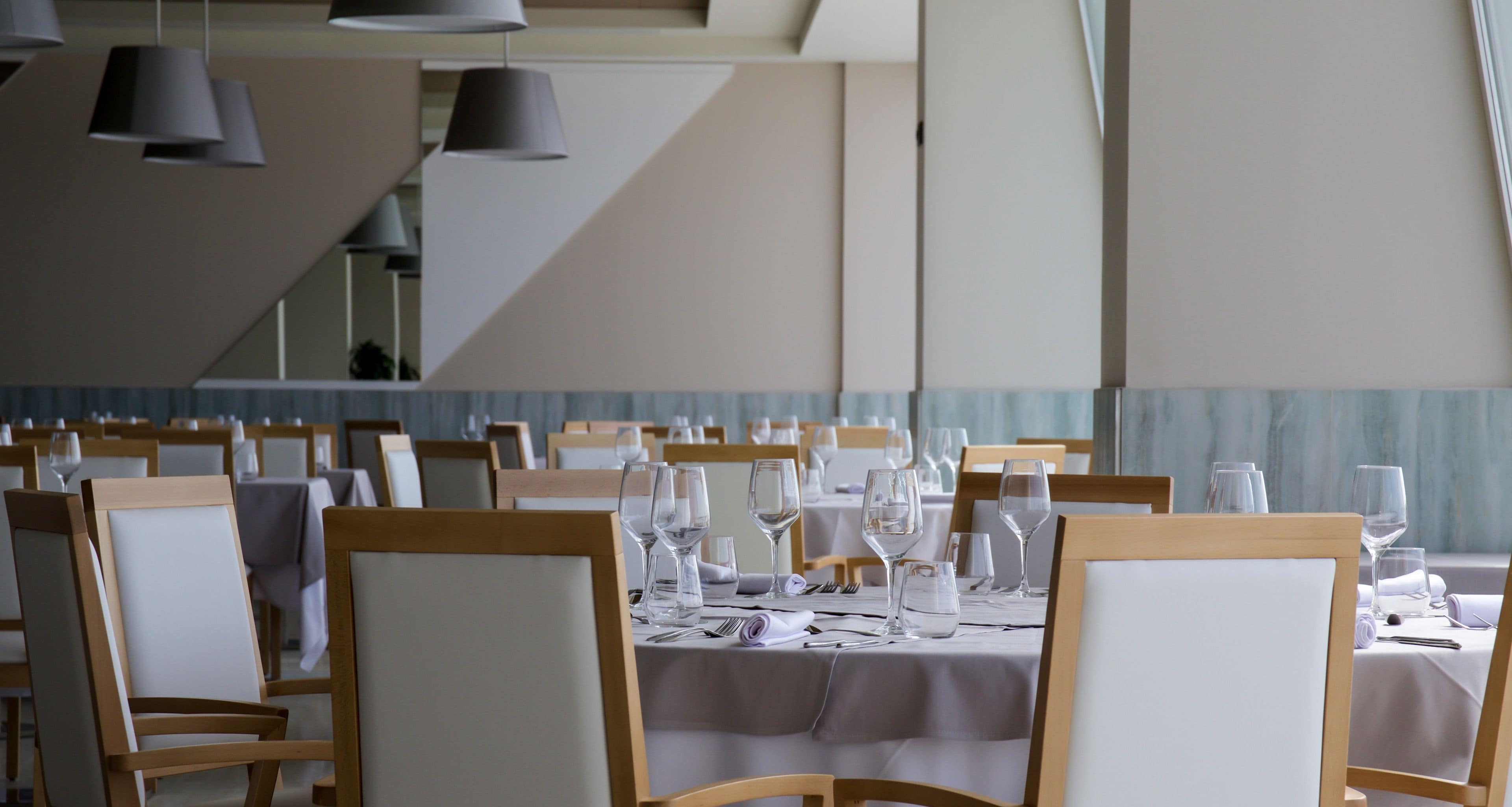 A restaurant with multiple tables set for dining, each with chairs and table settings including wine glasses and cutlery.