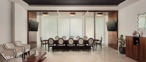 A modern conference room with a long table, chairs, a coffee table, and a TV screen.