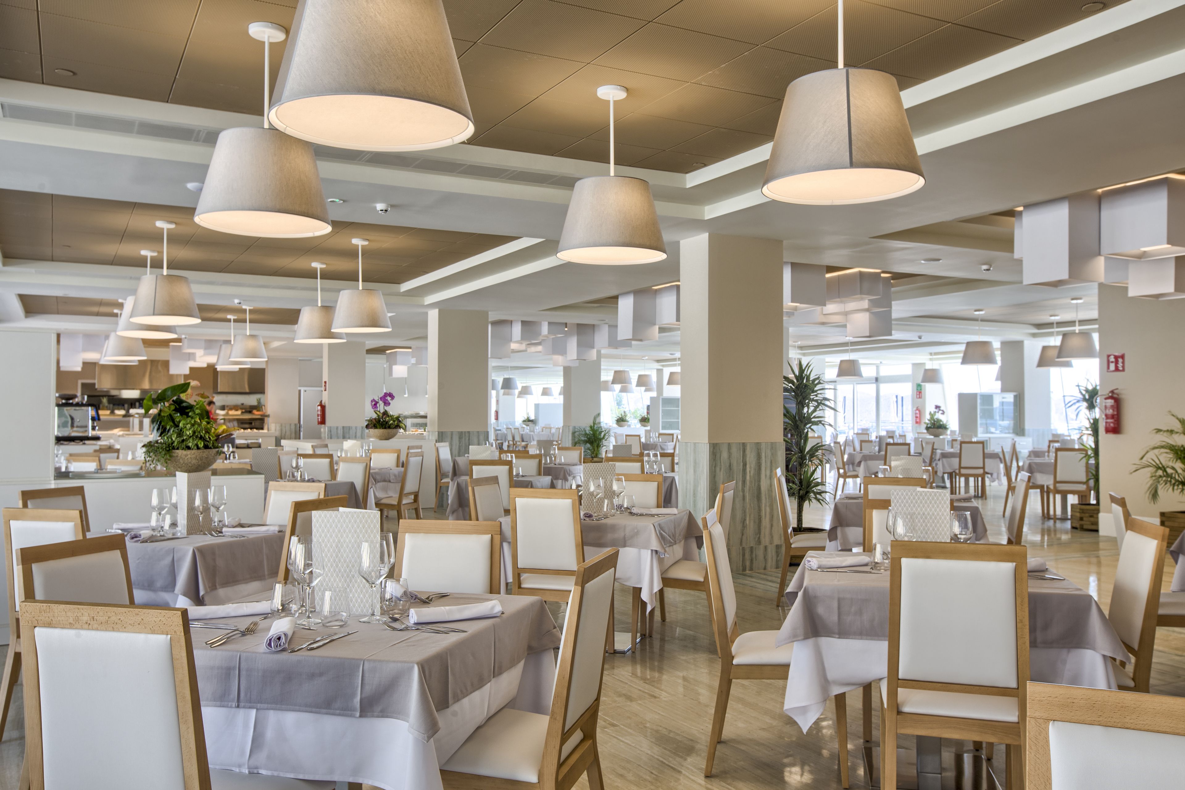 A spacious dining area with multiple tables and chairs, large pendant lights, and a modern ceiling design.